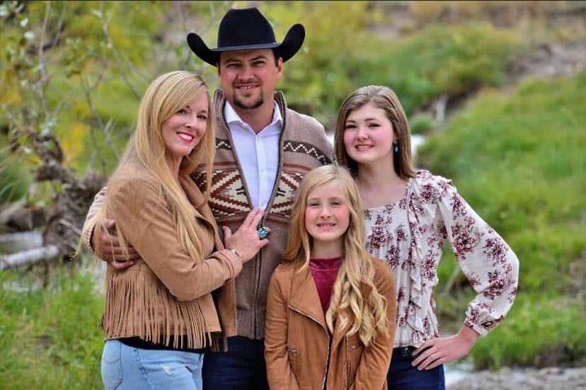 The Randall family together outdoors beside a creek, Anthony in a black hat with his wife and two daughters