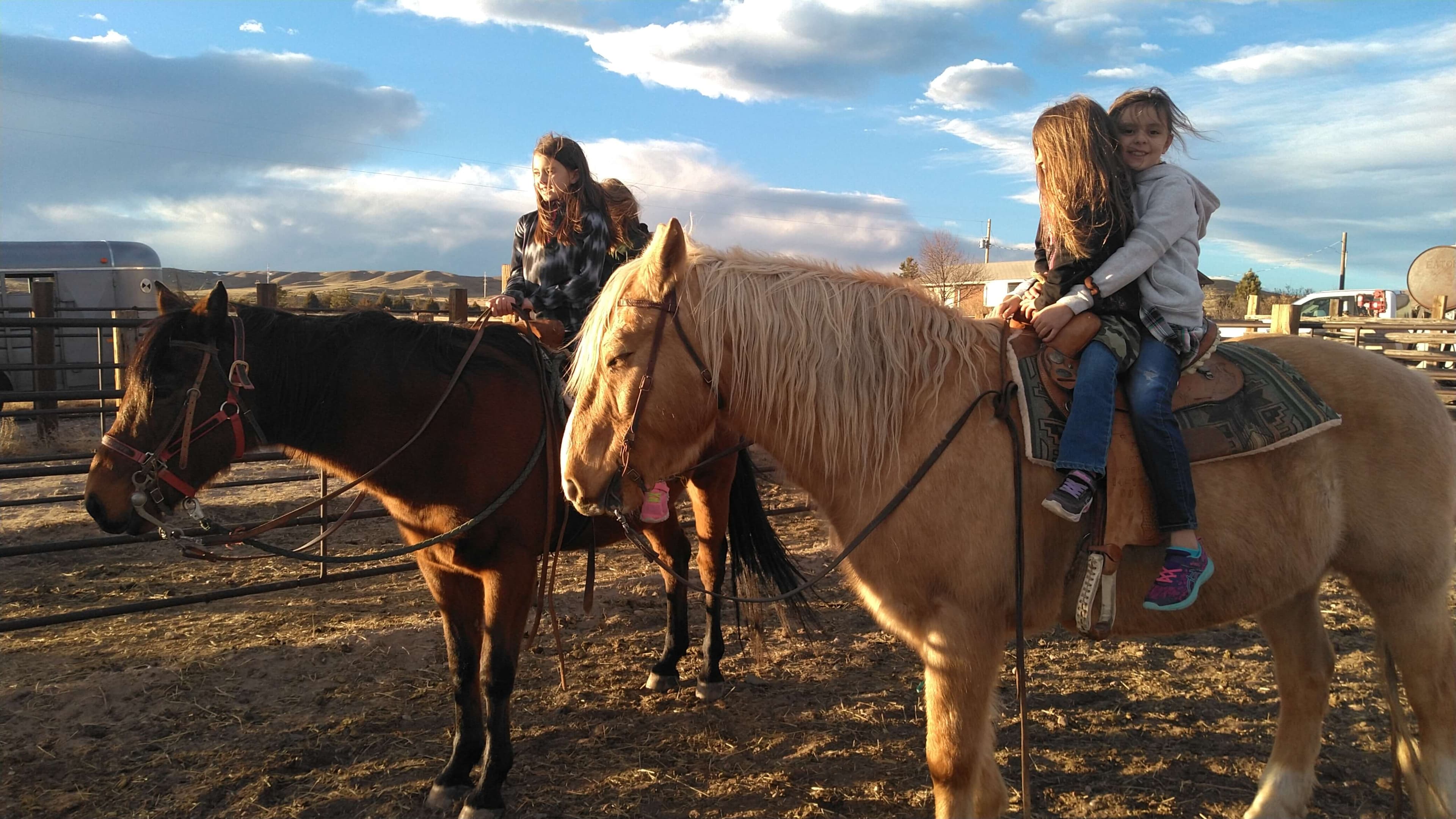 Three children on horseback in the ranch corral, with hills behind them