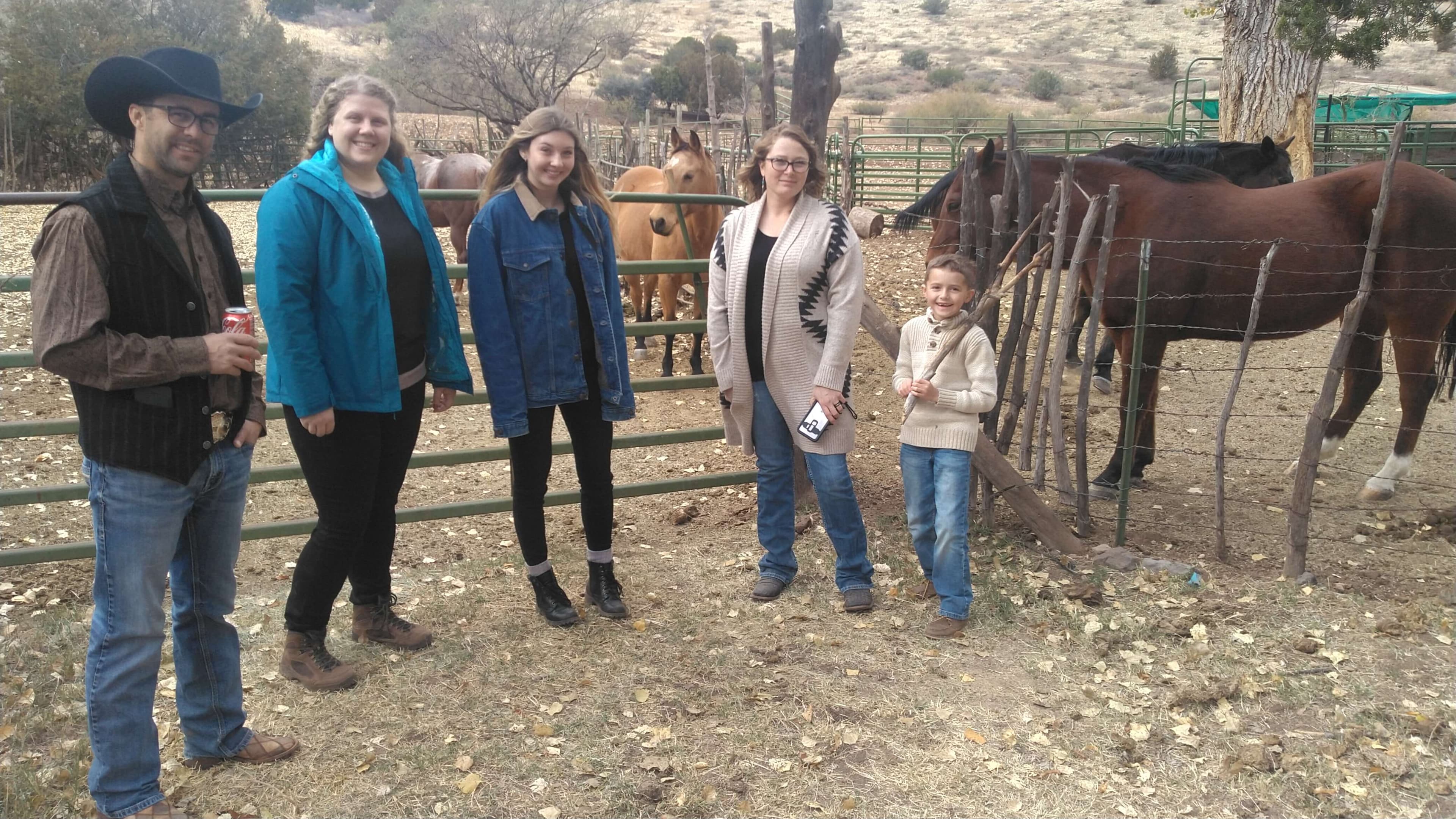 The Birkemeyer family standing along a corral fence beside their horses